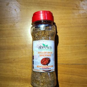 A transparent bottle with a red cap containing a blend of curry, thyme, rosemary, bay leaves, ginger, garlic and turmeric, for jollof rice.